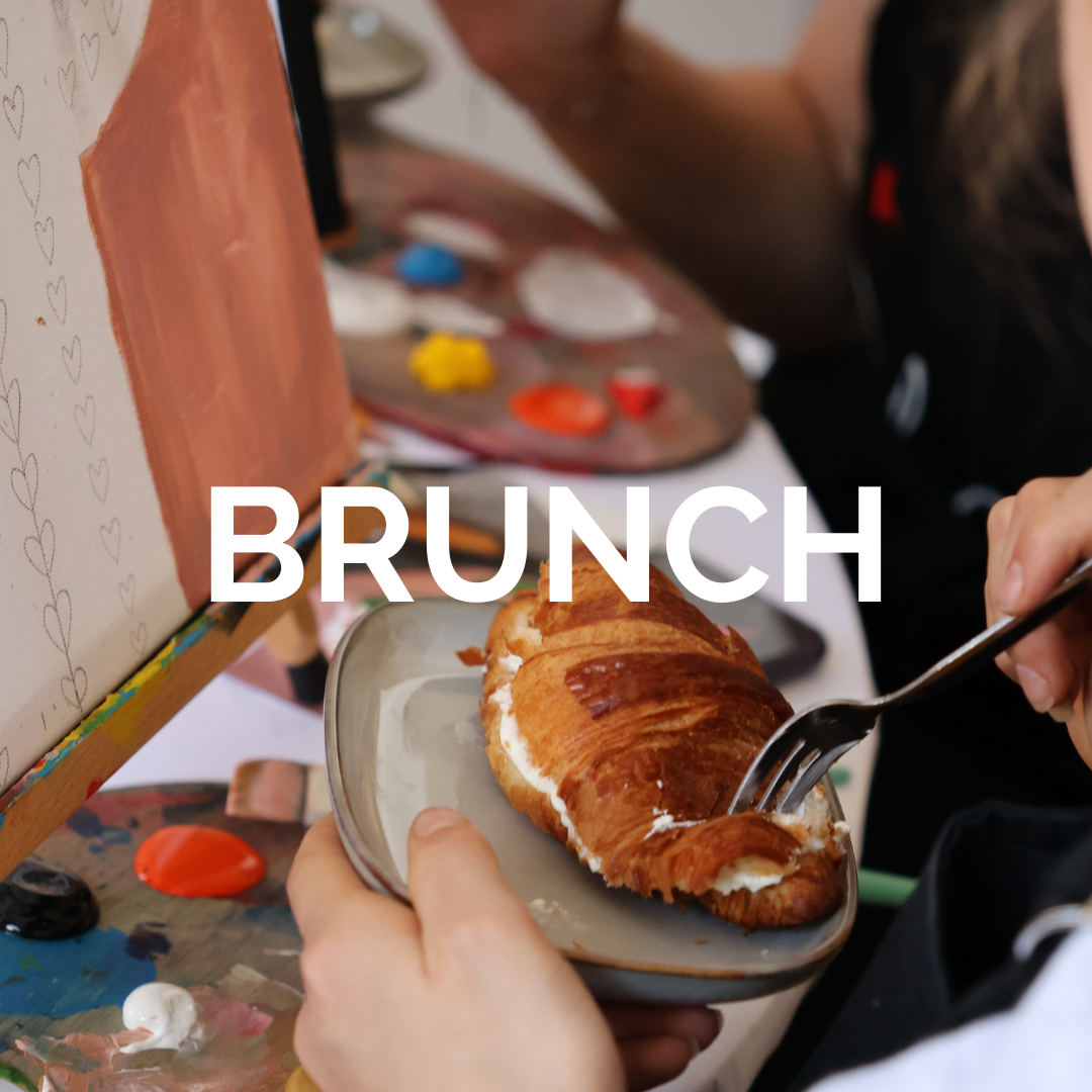 Ruka drží talíř, na kterém je položen croissant, vedle jsou malířské potřeby a plátno, text BRUNCH.